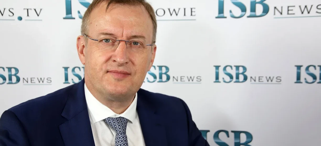 Pracownik umysłowy w garniturze, koszuli i okularach stojący przed telewizorem. Słowa kluczowe: Okulary, Opieka nad wzrokiem, Ubranie formalne, TV WS.